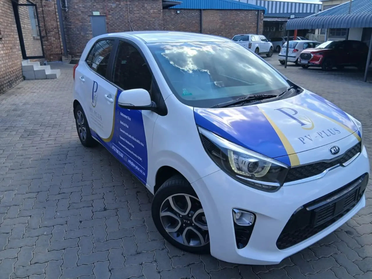 Front three-quarter view of a white Kia Picanto with blue, white and gold PV Plus branding