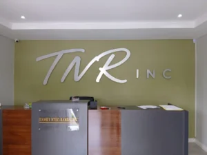 Dimensional TNR INC reception lettering on an olive-green office wall